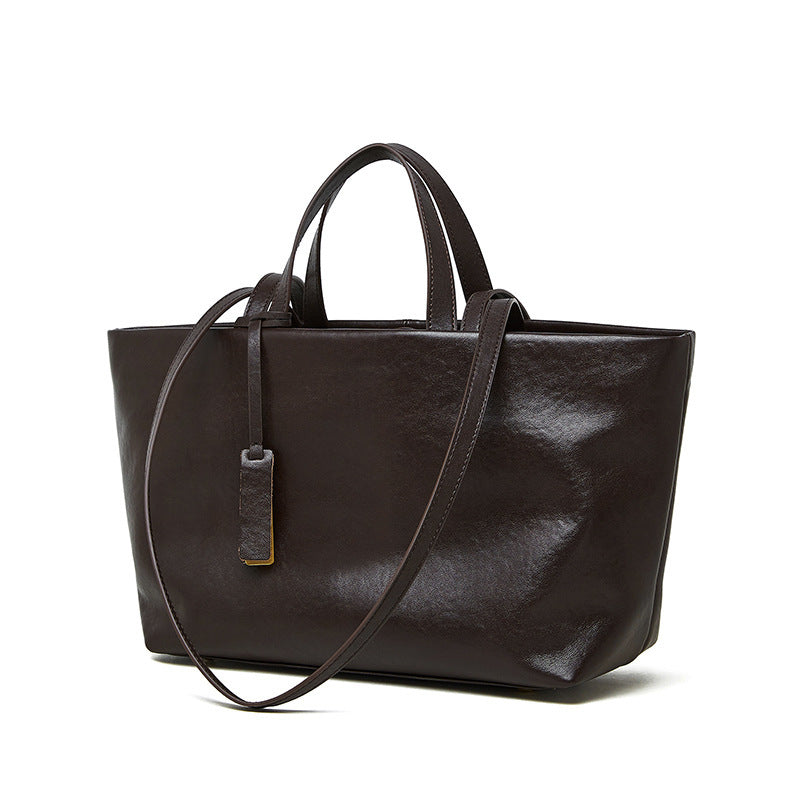 Dark brown leather tote bag with a shoulder strap on a white background
