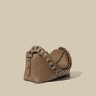 Brown leather handbag with braided handle on a beige background