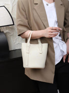 Person holding a white handbag with a neutral background