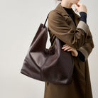 Person holding a brown leather handbag against a neutral background