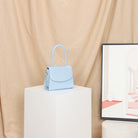 Light blue handbag on a white pedestal with a beige curtain background