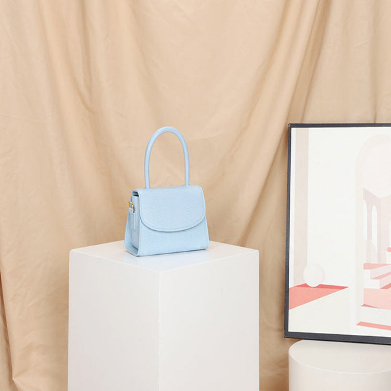 Light blue handbag on a white pedestal with a beige curtain background