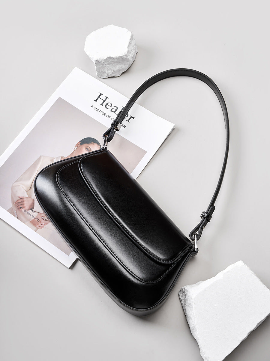 Black handbag on a light gray surface with a magazine underneath