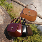 Three leather handbags in brown, red, and black hanging on a branch with a natural background.