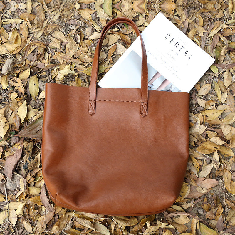 Brown leather tote bag with a magazine on a bed of dried leaves
