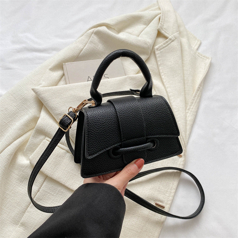 Black handbag held by a hand on a white background with a light-colored fabric.