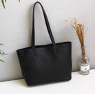 Black handbag on a white surface with green leaves and a vase in the background