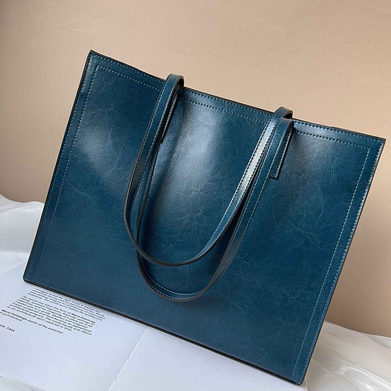 Blue leather tote bag on a white surface with a beige background