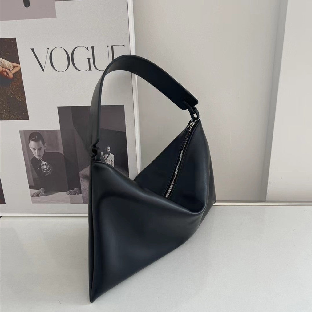 Black handbag on a white surface with a magazine in the background