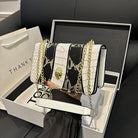 White handbag with black snake print and gold chain held by a person, displayed in an open box.