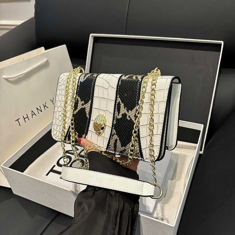 White handbag with black snake print and gold chain held by a person, displayed in an open box.