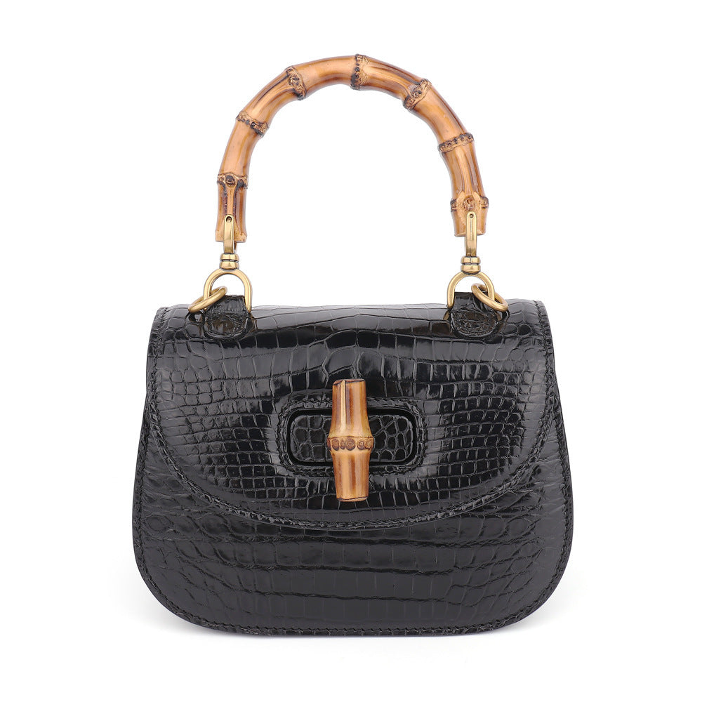 Black crocodile skin handbag with gold bamboo handle on a white background
