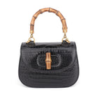 Black crocodile skin handbag with gold bamboo handle on a white background