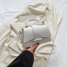 White handbag held by a hand on a light-colored fabric background