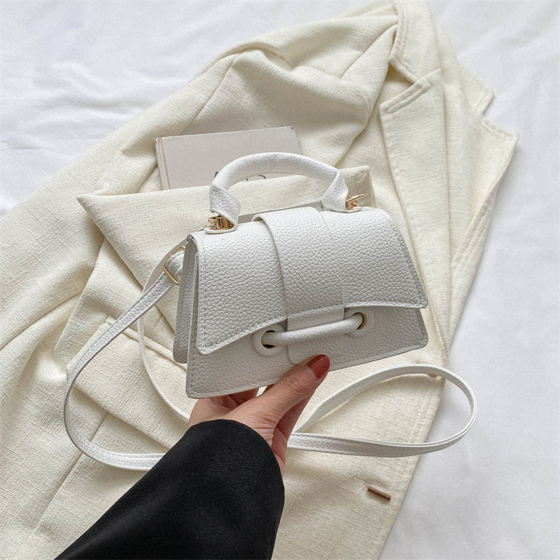 White handbag held by a hand on a light-colored fabric background
