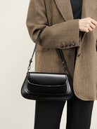 Person wearing a brown coat holding a black handbag against a neutral background