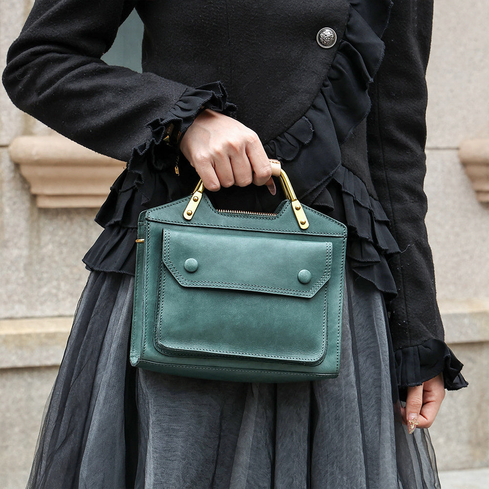 Person holding a green handbag with a black coat and gray skirt.