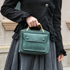 Person holding a green handbag with a black coat and gray skirt.