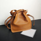 Brown leather bucket bag on a black surface with a white background