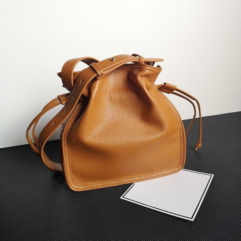 Brown leather bucket bag on a black surface with a white background