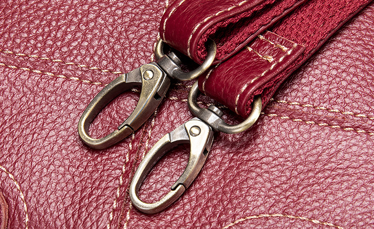 Close-up of a red leather strap with metal clasps on a textured red surface