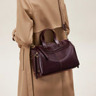 Person wearing a beige coat holding a purple handbag against a neutral background