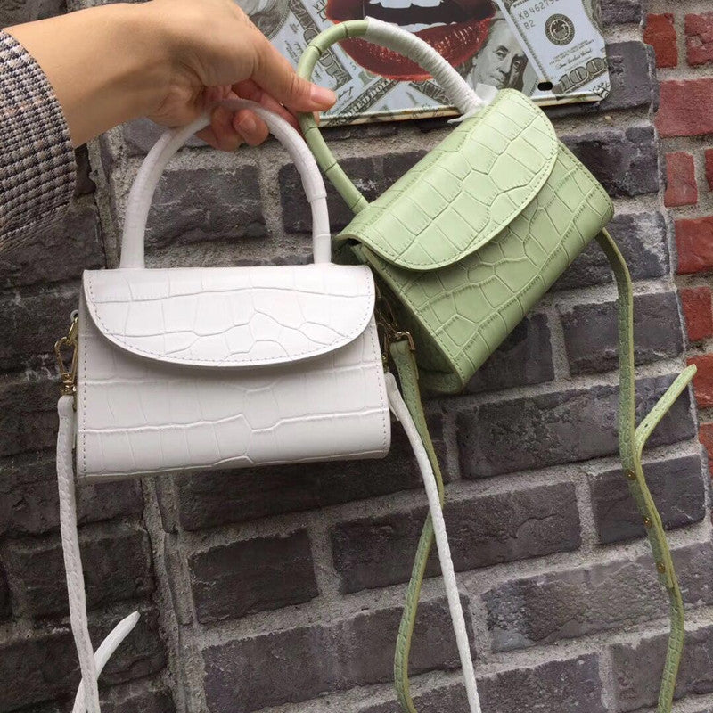 Two handbags, one white and one green, held against a brick wall.