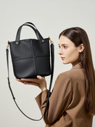 Woman holding a black handbag against a neutral background