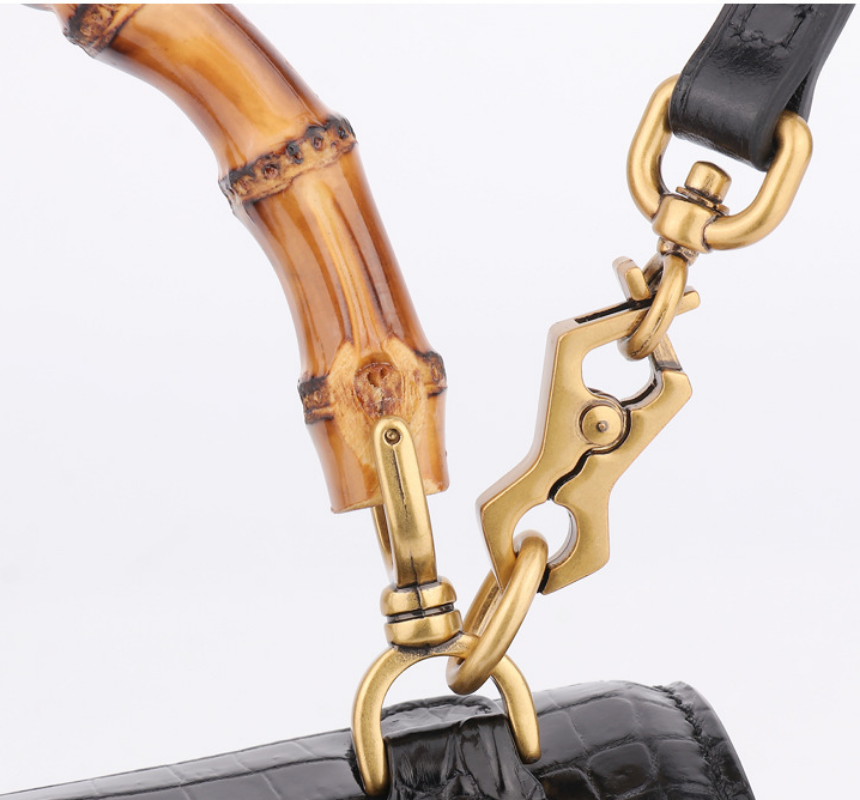 Close-up of a gold handbag clasp with a bamboo handle on a white background