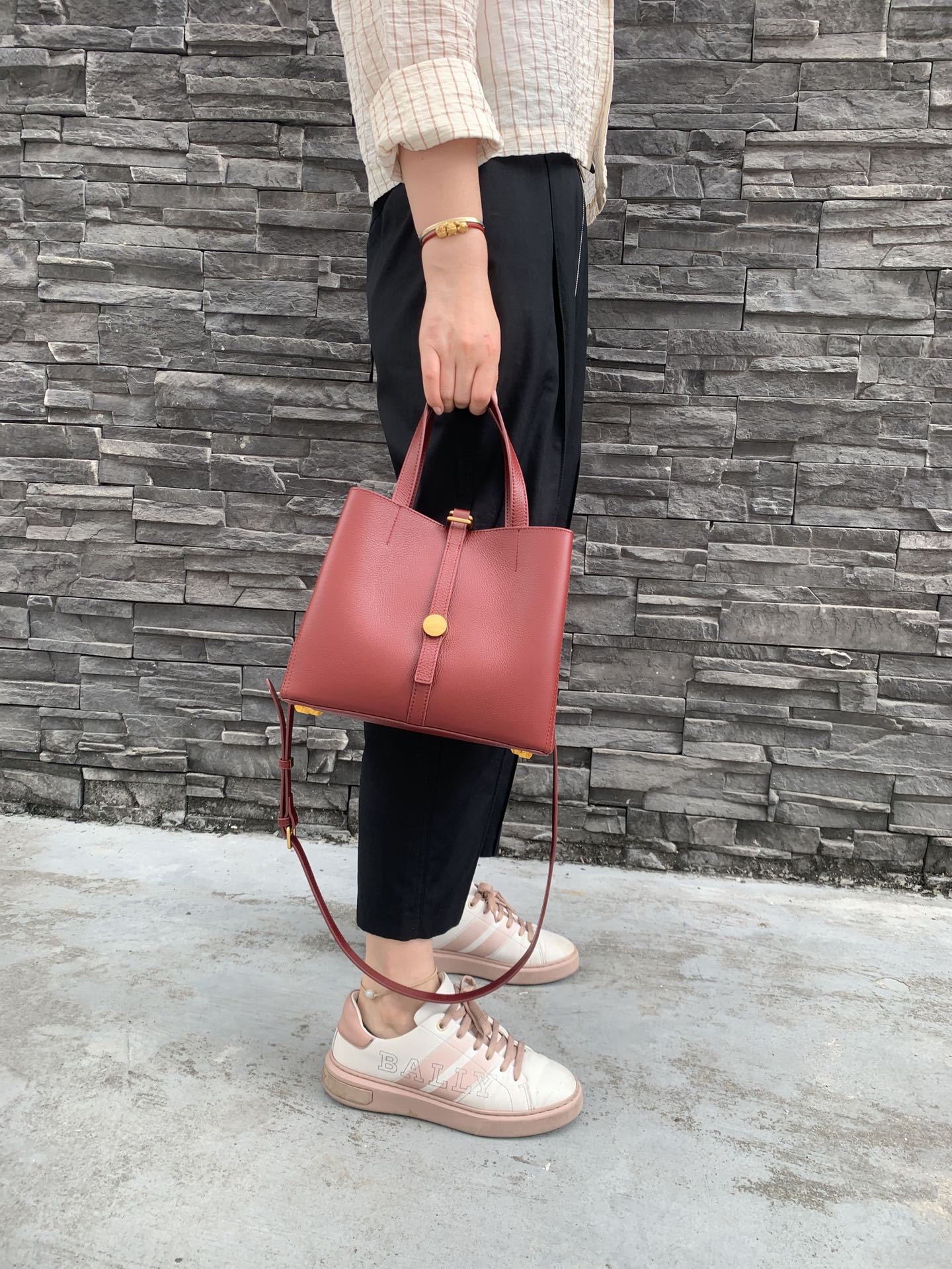 Person holding a pink handbag against a stone wall background