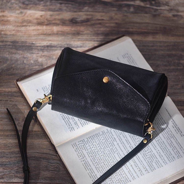 Black leather clutch bag on an open book with a wooden background