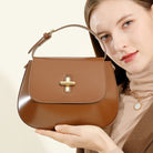 Woman holding a brown handbag with a gold clasp against a beige background