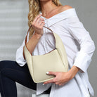 Woman holding a beige handbag against a neutral background