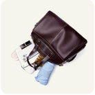 Brown leather briefcase with a smartphone, glasses, and blue umbrella inside on a white background
