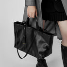 Person holding a black leather tote bag against a neutral background