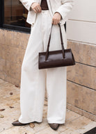 Person wearing a white outfit with a brown handbag outdoors.
