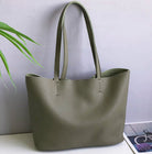 Green handbag on a white surface with a plant and magazine in the background