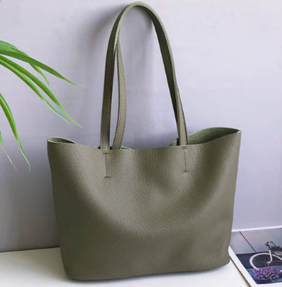 Green handbag on a white surface with a plant and magazine in the background