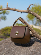 Brown leather handbag with a gold clasp on a rock with a natural background