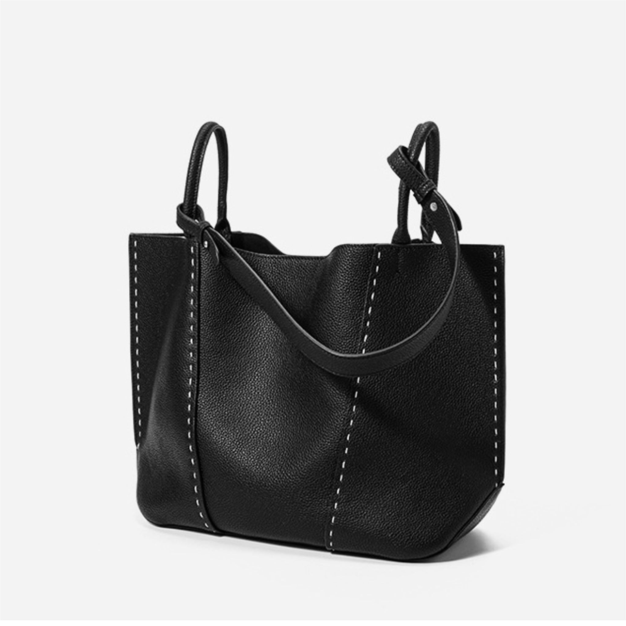 Black leather handbag with handle and shoulder strap on a light gray background