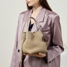 Woman holding a beige handbag against a plain background