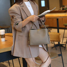 Person in a beige suit holding a brown leather handbag in a cafe setting