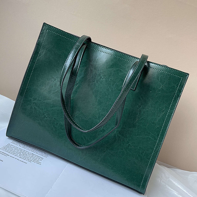 Green leather tote bag on a white surface with a beige background