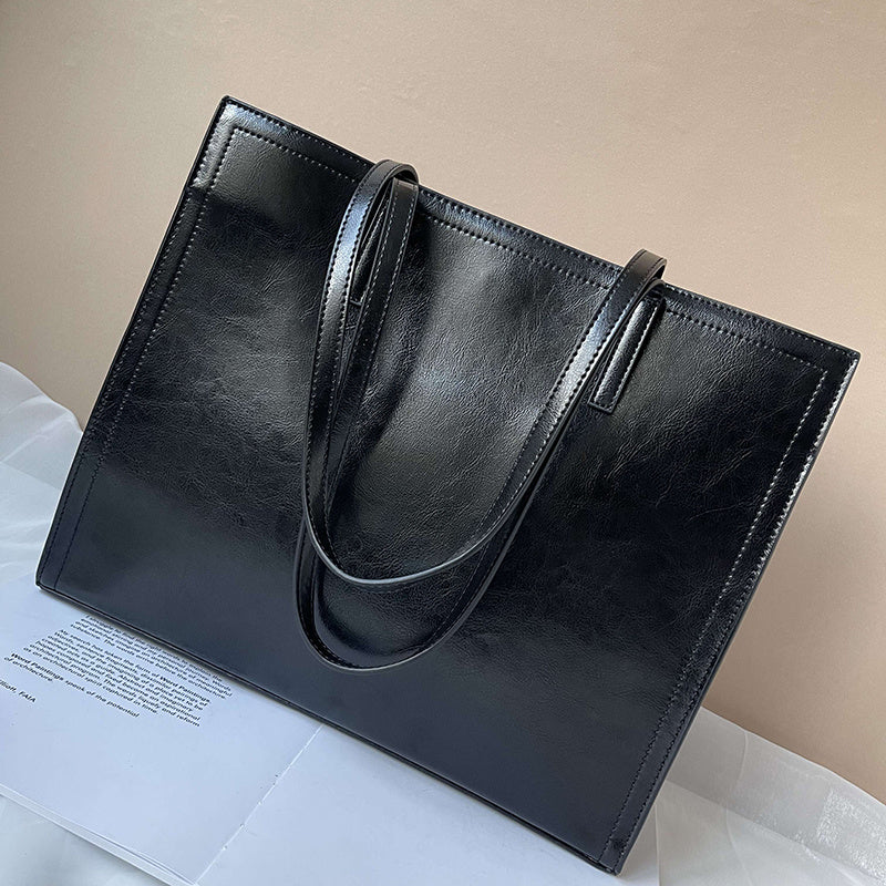 Black leather tote bag on a light surface with a beige background