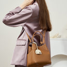 Person wearing a light purple coat holding a brown handbag against a neutral background
