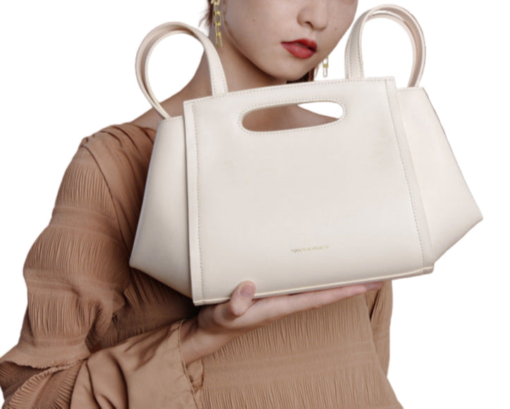 White handbag held by a person against a white background