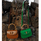 Brown and green handbags with bamboo handles against a stone wall.