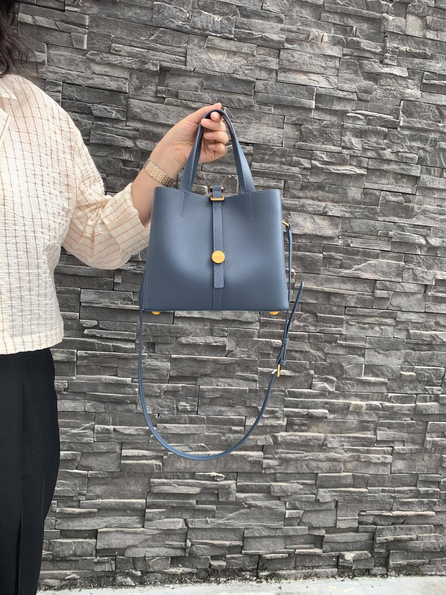 Person holding a blue handbag against a stone wall