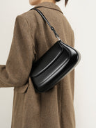 Person wearing a brown coat with a black shoulder bag on a plain background