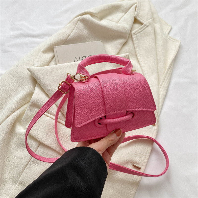 Pink handbag held by a hand with a light-colored coat and paper in the background